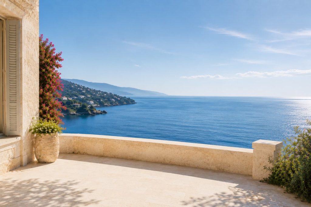 Co-living abroad for women over 50: Sunny stone terrace of a Mediterranean seaside villa with bougainvillea, overlooking the deep-blue sea and a coastal hillside.