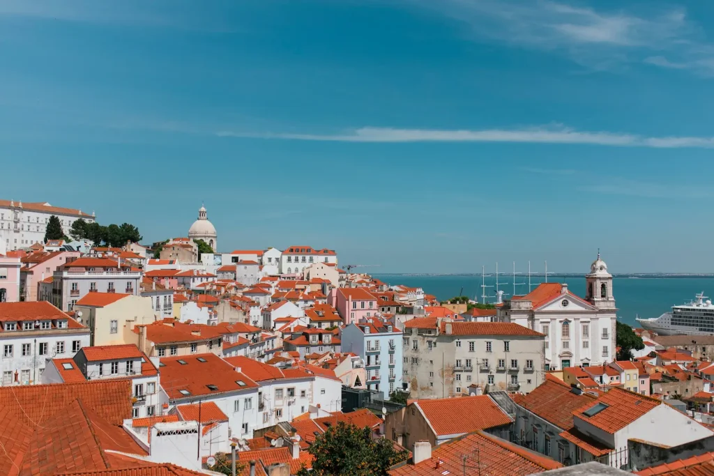 Portugal for solo women over 50 Sunny view over Lisbon's red-tiled Alfama rooftops to the Tagus River, with the National Pantheon dome and a white church.