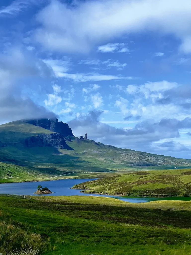 A magnificent landscape view of the Old Man of Storr rock formation and the calm waters of Loch Fada on the Isle of Skye, illustrating beautiful Scotland solo travel for women over 50.