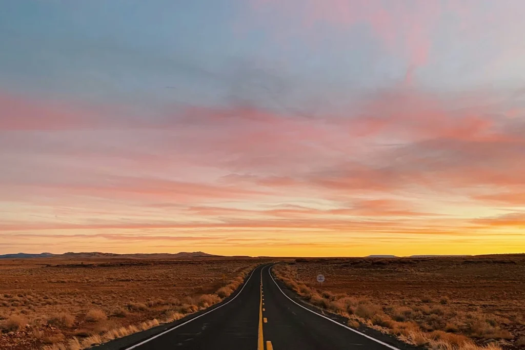 An open road stretching toward a sunset horizon — solo travel for women over 50.