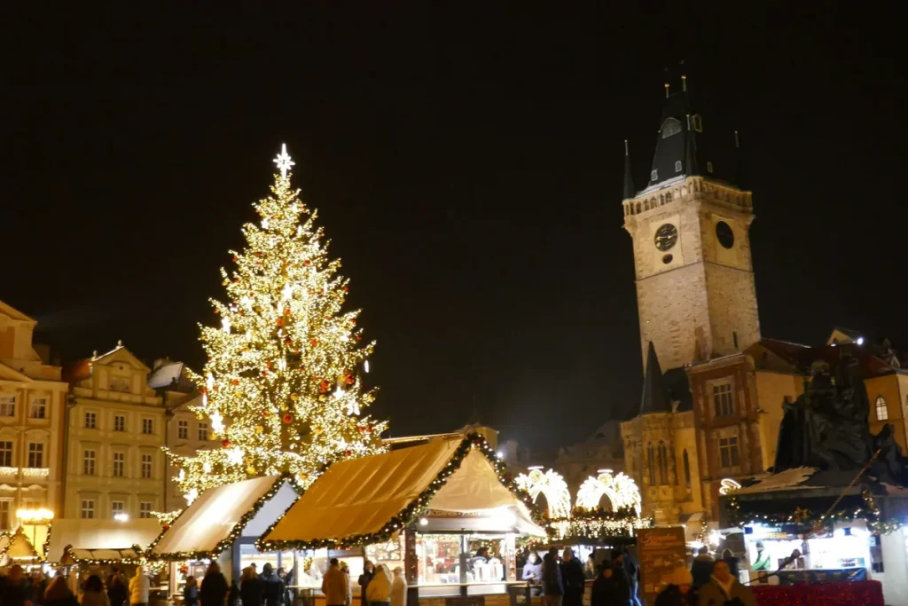 Prague Christmas markets over 50: the old town at dusk, a lit Christmas tree and glowing wooden chalets beneath the city's Gothic spires